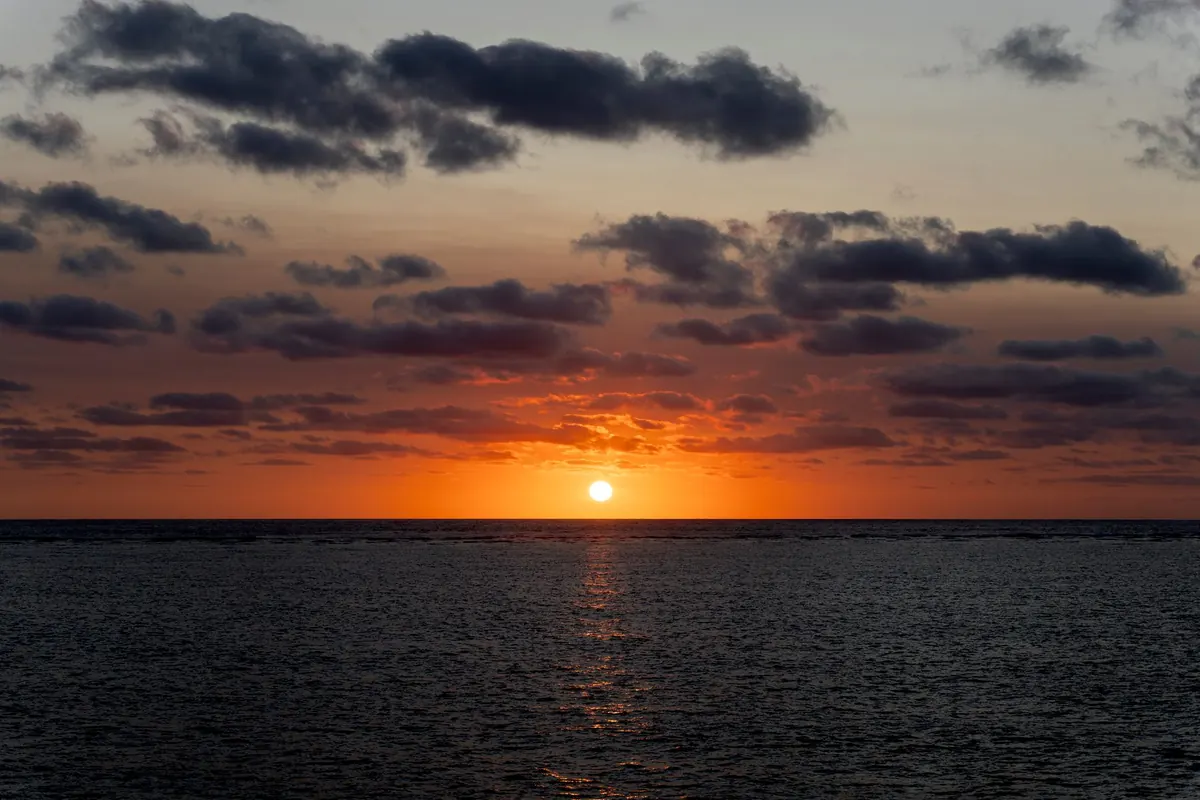 The sun sinking into a dark sea off Cairns under bands of cloud, with an orange glow along the horizon.